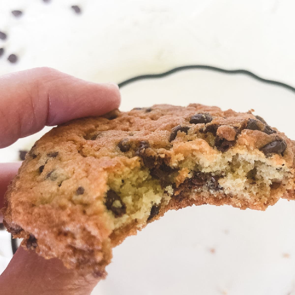 hand holding chocolate chip cookie with one bite taken out.