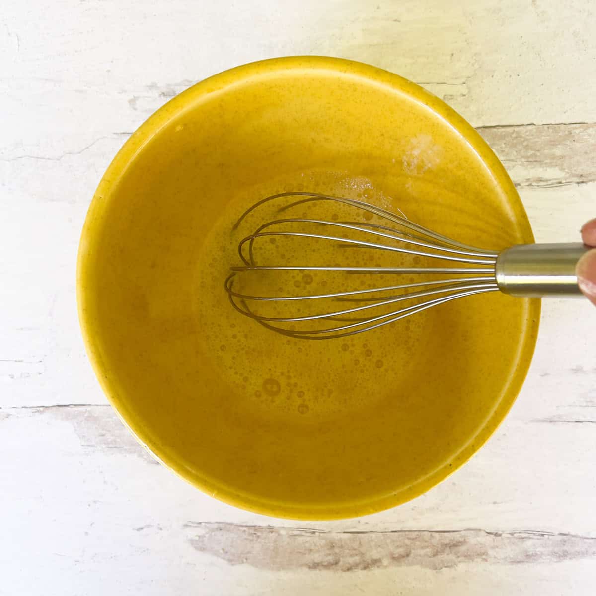 Whipped eggs whites in yellow bowl with whisk.