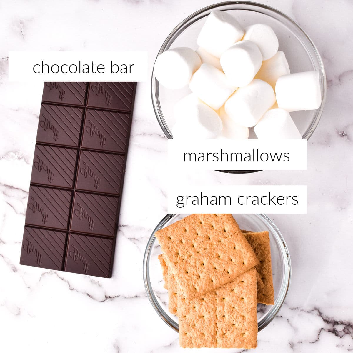 Graham crackers, marshmallows, and chocolate bar on marble countertop.