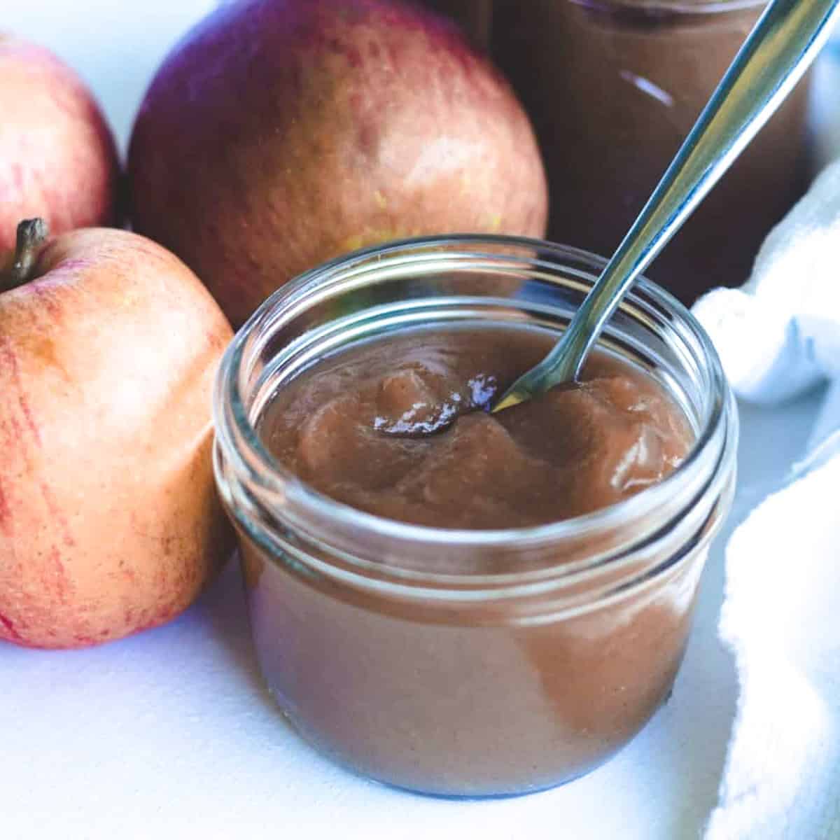 Small jar of homemade apple butter with apples in background.