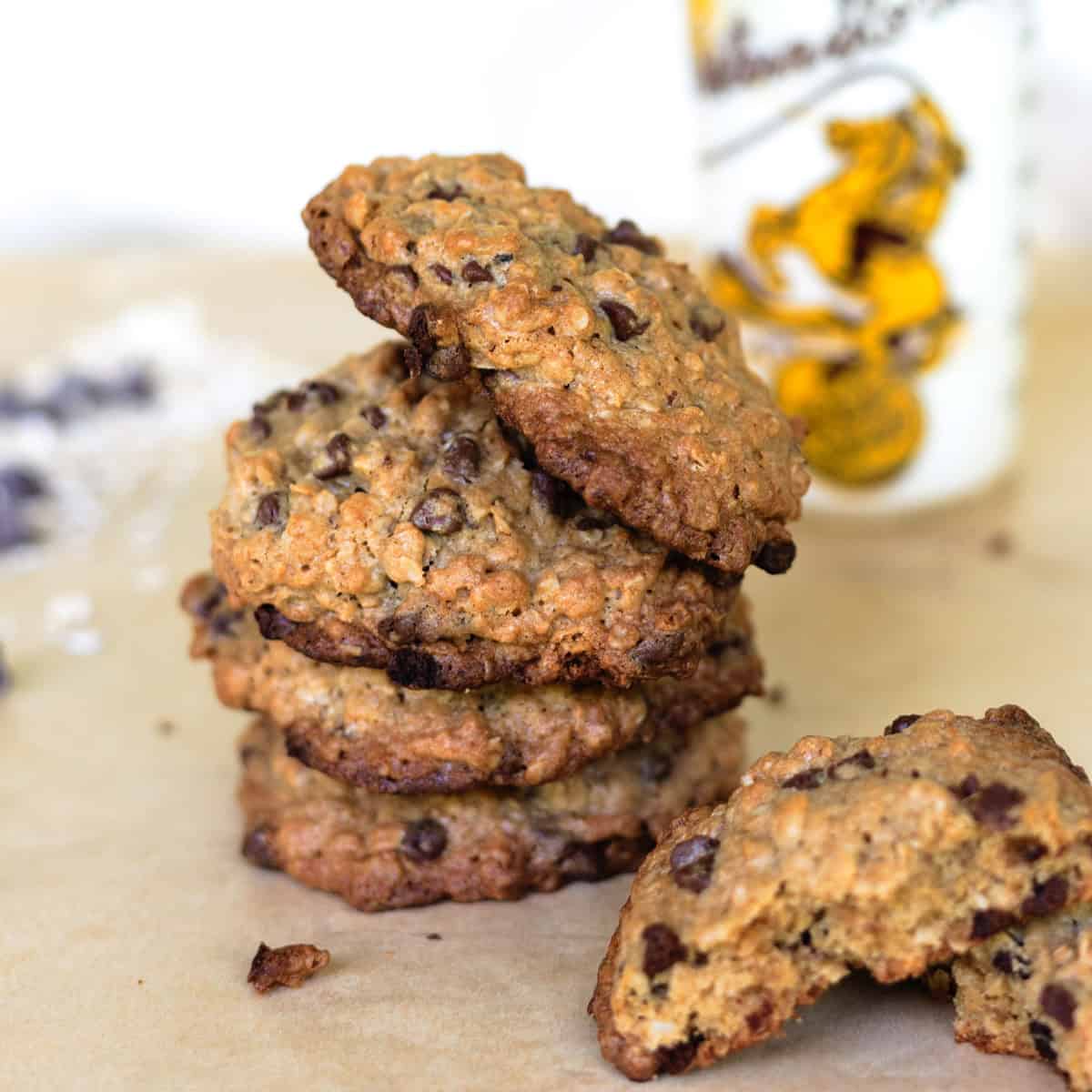 Stack of cowboy cookies on parchment paper with glass of milk.