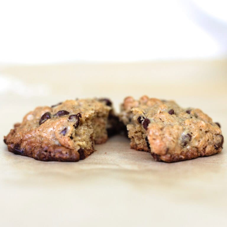 One cowboy cookie split in half on parchment paper.