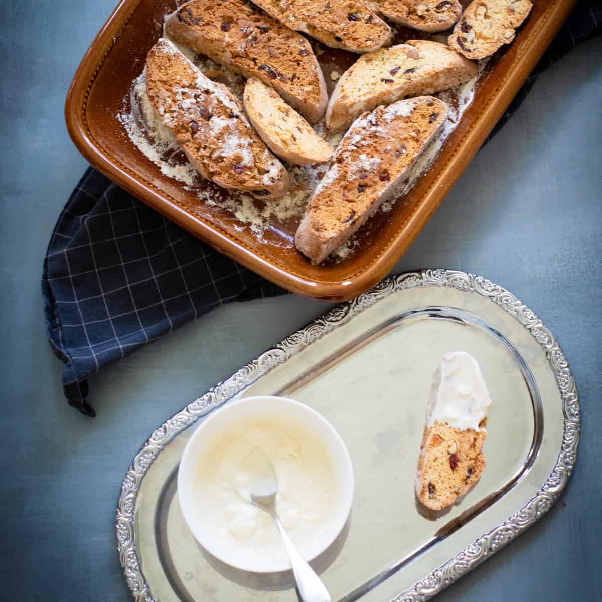 Biscotti in baking pan with melted white chocolate on tray.