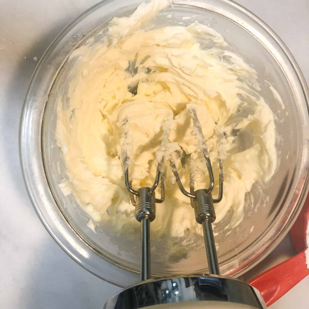 Cream cheese cookie dough in bowl with hand mixer.