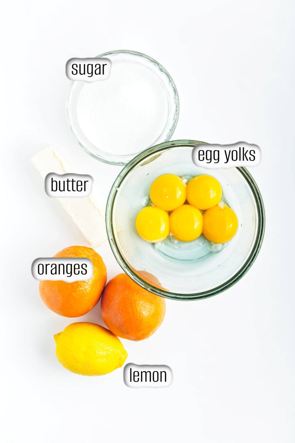 Eggs yolks, butter, sugar, lemon and oranges on countertop.