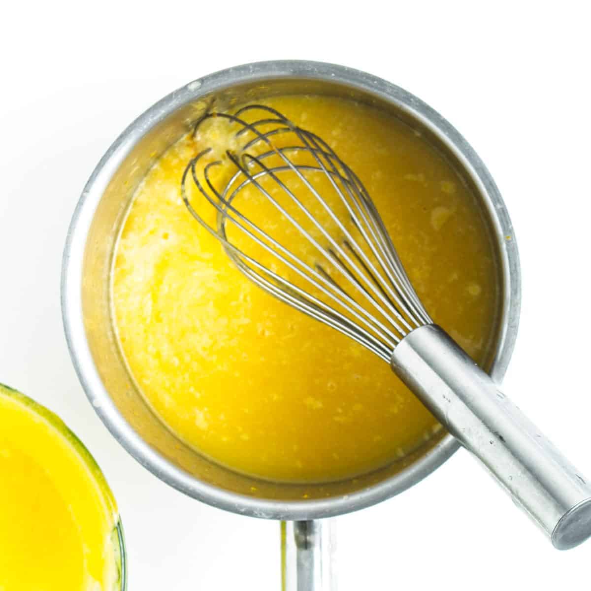 Orange curd and whisk in saucepan.