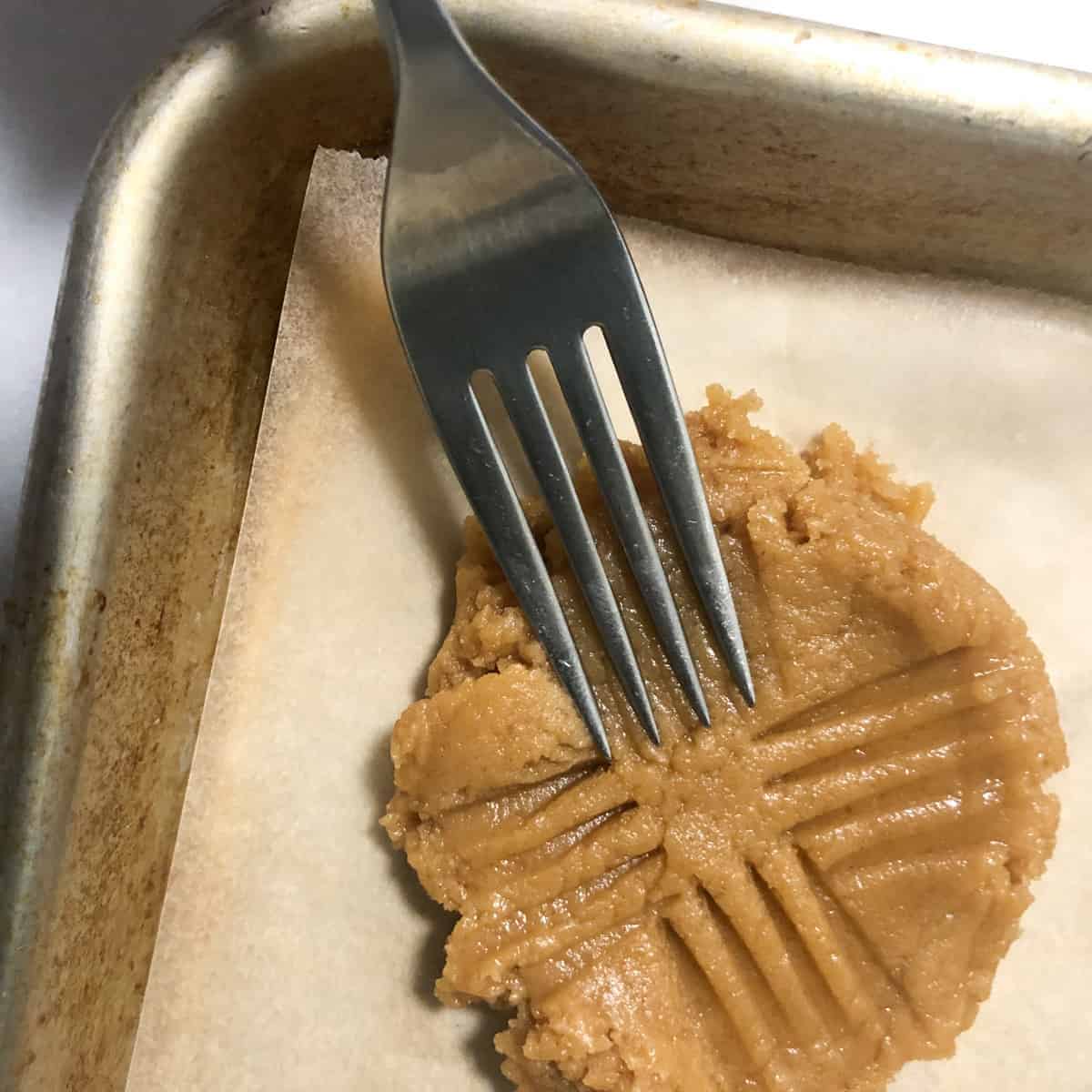 Fork making pattern on peanut butter cookie dough.